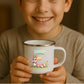 Kind hält weiße Emaille Kindertasse mit silbernem Rand – personalisierte Tasse mit Namen und süßem Motiv