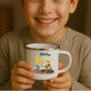 Kind hält weiße Emaille Kindertasse mit silbernem Rand – personalisierte Tasse mit Namen und süßem Motiv
